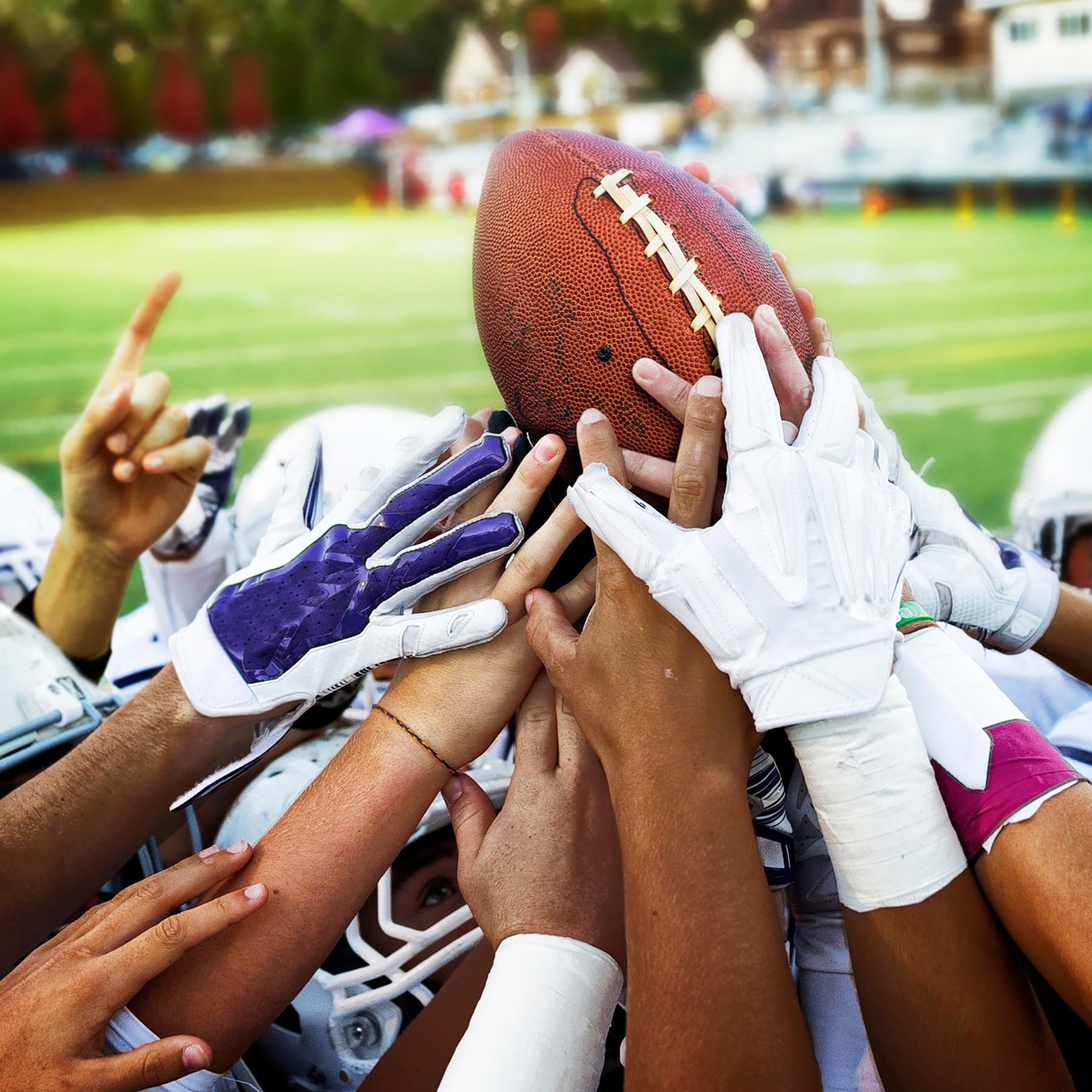 Football players' hands reaching together for a football during a game